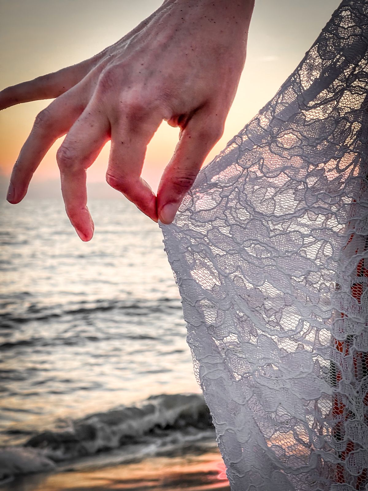 Main effleurant une dentelle à contre-jour devant la mer