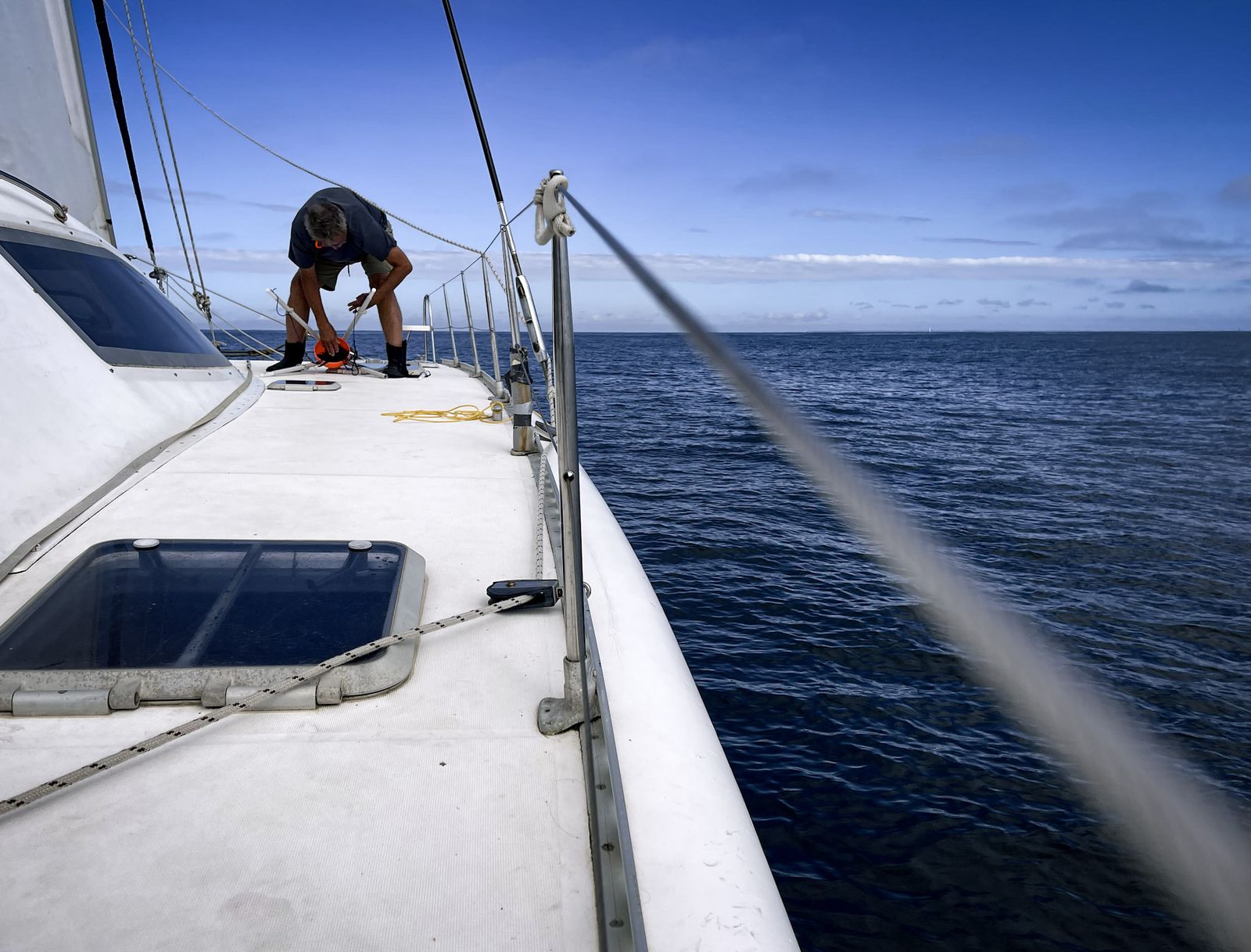 Marin à l’avant d’un voilier, mer d’un bleu profond