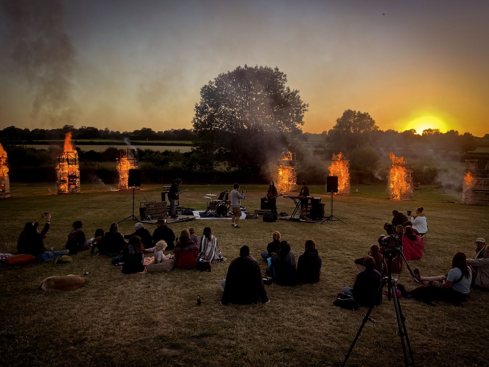 Public assis dans un champ devant des tours de bois en feu